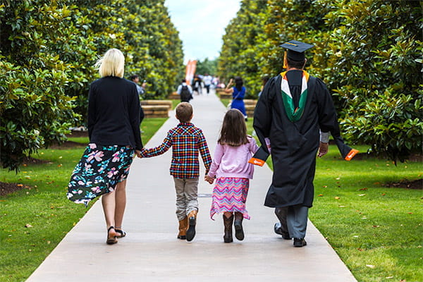 MBA graduate in cap and gown with family on the UT Dallas campus